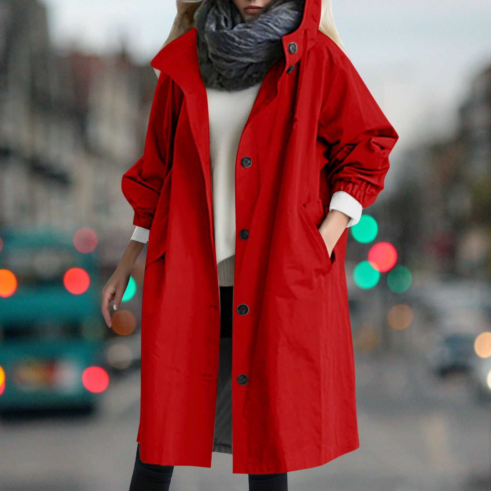 Cappotto rosso donna, lungo e oversize, con bottoni neri e tasche, indossato su maglione bianco e sciarpa grigia, sfondo urbano sfocato.