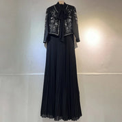 Abito lungo nero elegante con giacca ricamata, dettagli floreali bianchi, gonna plissettata. Moda donna, abbigliamento formale, stile sofisticato.