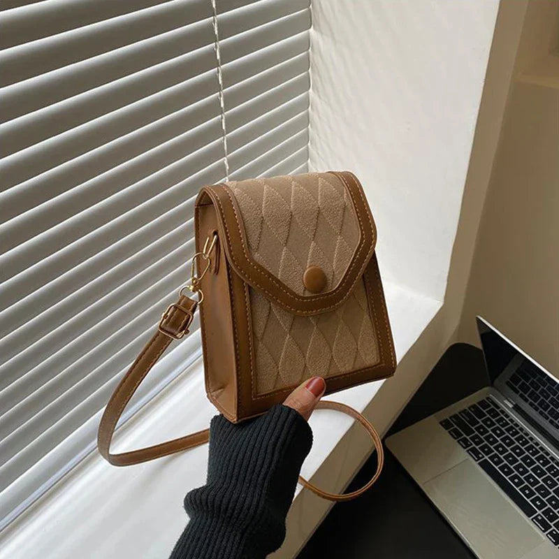 Borsa a tracolla marrone chiaro con motivo a rombi, chiusura a bottone, accanto a laptop su scrivania. Accessorio moda elegante e pratico.