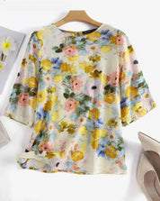 Blusa floreale donna in chiffon, maniche a tre quarti, colori pastello, sfondo bianco. Elegante e leggera, perfetta per la primavera.