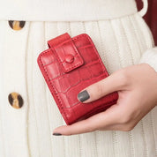 Portafoglio rosso in pelle con motivo coccodrillo, chiusura a bottone, tenuto in mano. Accessorio moda elegante per donna.