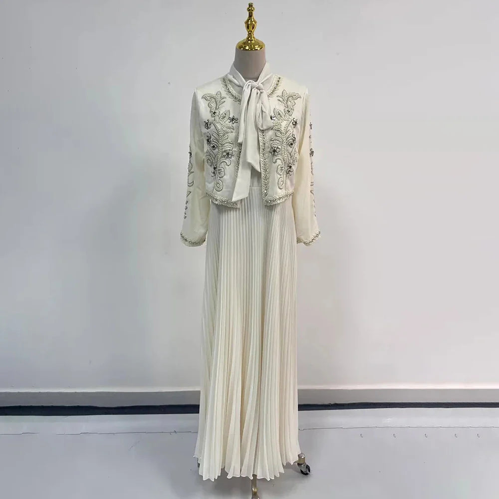 Abito lungo bianco elegante con giacca ricamata, maniche lunghe, colletto con fiocco, gonna plissettata. Perfetto per cerimonie e occasioni speciali.