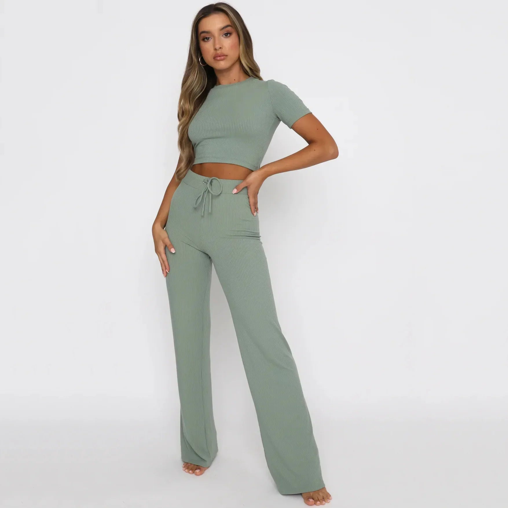 Modella indossa completo coordinato verde salvia, top corto e pantaloni a vita alta. Abbigliamento donna elegante, moda casual, tendenza 2023.