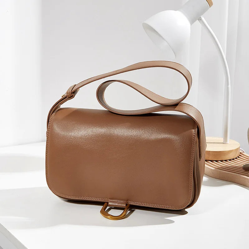 Borsa a tracolla in pelle marrone su tavolo bianco, design elegante e minimalista, con lampada moderna sullo sfondo. Accessorio moda donna.