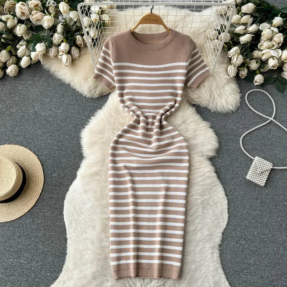 Abito a righe beige e bianche su tappeto peloso bianco, circondato da rose bianche e accessori moda. Elegante, casual, perfetto per l'estate.