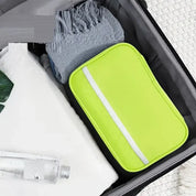 Valigia aperta con beauty case verde lime, asciugamano bianco, bottiglia trasparente e sciarpa grigia. Accessori da viaggio organizzati.
