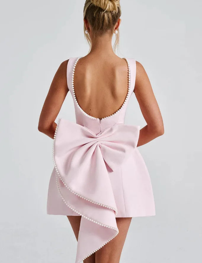 Abito rosa elegante con fiocco posteriore, scollatura profonda, dettagli perle, moda donna, abbigliamento da sera, stile sofisticato.