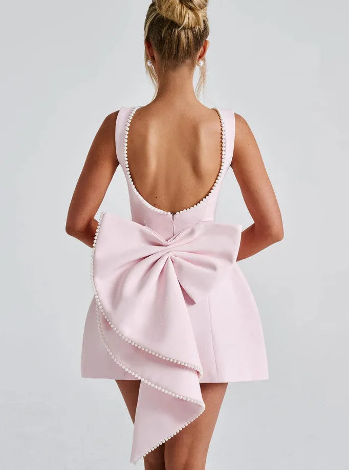 Abito rosa elegante con fiocco posteriore, scollatura profonda, dettagli perle, moda donna, abbigliamento da sera, stile sofisticato.