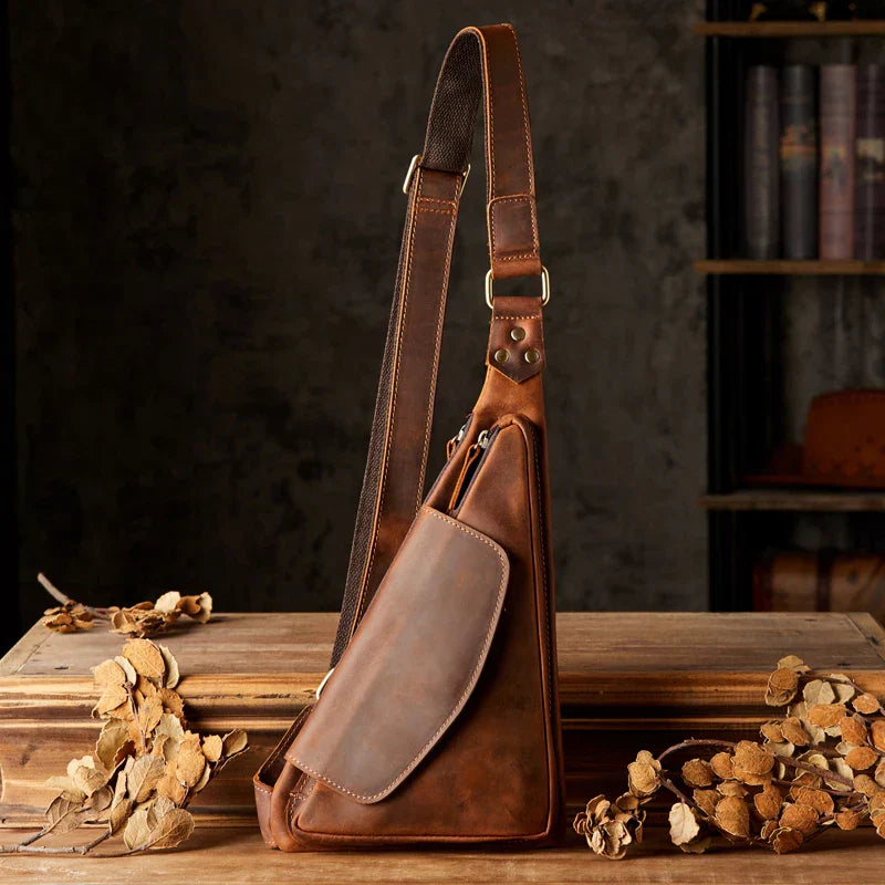 Borsa a tracolla in pelle marrone vintage su tavolo di legno, design elegante e pratico, ideale per uomo, accessorio moda autunno.