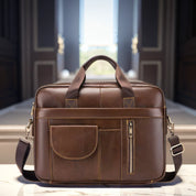 Borsa ventiquattrore in pelle marrone con tasche frontali e tracolla regolabile, posizionata su un tavolo in un ambiente elegante.