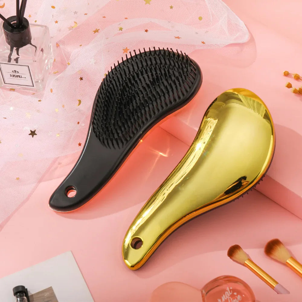 Spazzole per capelli districanti, una nera e una dorata, su sfondo rosa con accessori di bellezza. Design ergonomico, setole morbide.