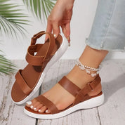 Sandali donna marroni con suola bianca, cinturino regolabile, indossati con jeans chiari e cavigliera. Scarpe estive eleganti e comode.