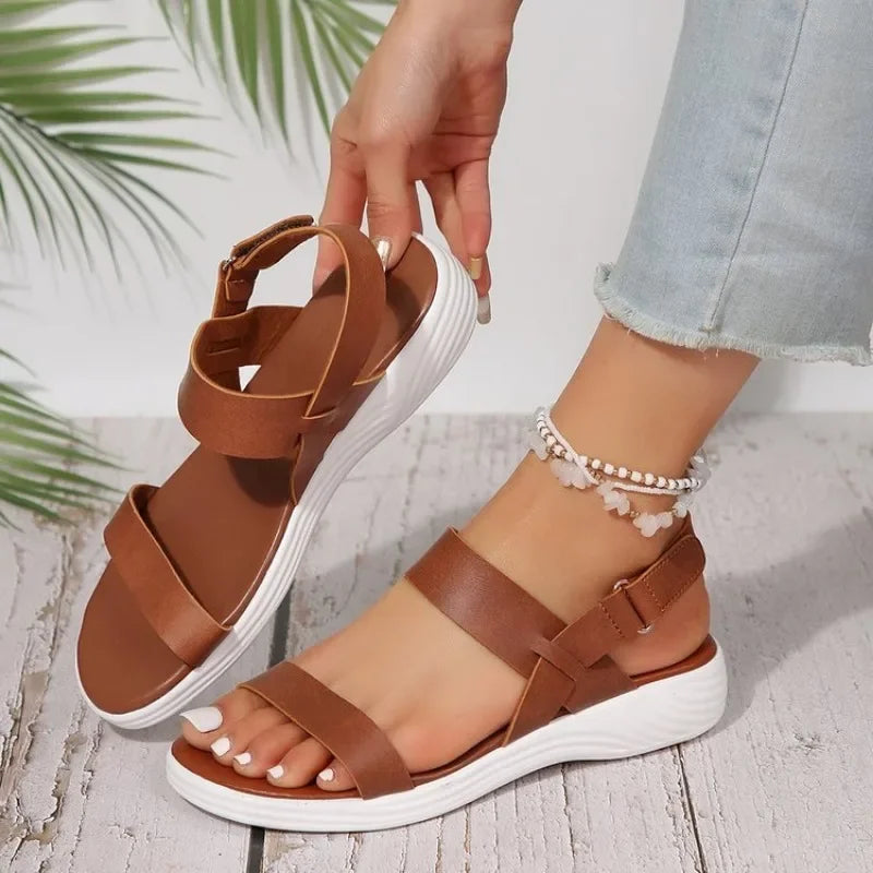 Sandali donna marroni con suola bianca, cinturino regolabile, indossati con jeans chiari e cavigliera. Scarpe estive eleganti e comode.