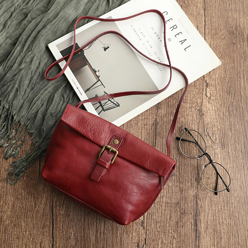 Borsa a tracolla in pelle rossa su tavolo di legno, accanto a occhiali e rivista. Elegante accessorio moda donna, stile casual chic.