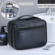 Borsa da toilette in pelle nera con zip, dimensioni 24.5x10x18.5 cm, accanto a rasoio e sapone da uomo. Ideale per viaggi e organizzazione bagno.