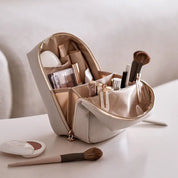 Astuccio trucco beige aperto su tavolo, con pennelli, rossetti e cosmetici. Organizer make-up elegante, ideale per viaggi e uso quotidiano.