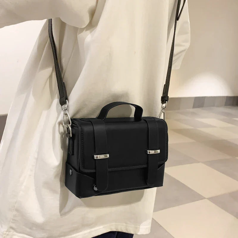 Borsa a tracolla nera in pelle, design elegante e compatto, indossata su camicia bianca. Accessorio moda unisex, ideale per uso quotidiano.