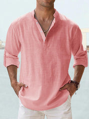 Camicia uomo in lino rosa, maniche lunghe arrotolate, colletto alla coreana, abbinata a pantaloni bianchi. Stile casual estivo elegante.