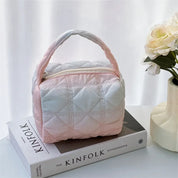 Borsa trapuntata rosa e bianca su libro "The Kinfolk", accanto a vaso con fiori bianchi. Design elegante, ideale per moda e accessori donna.