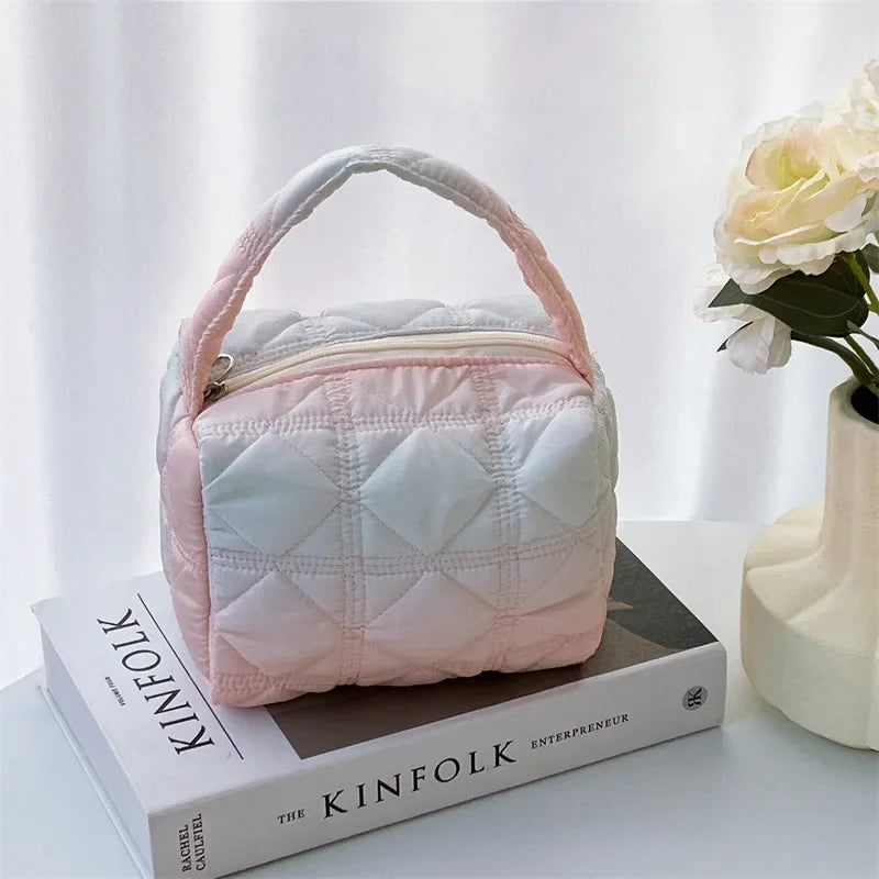 Borsa trapuntata rosa e bianca su libro "The Kinfolk", accanto a vaso con fiori bianchi. Design elegante, ideale per moda e accessori donna.