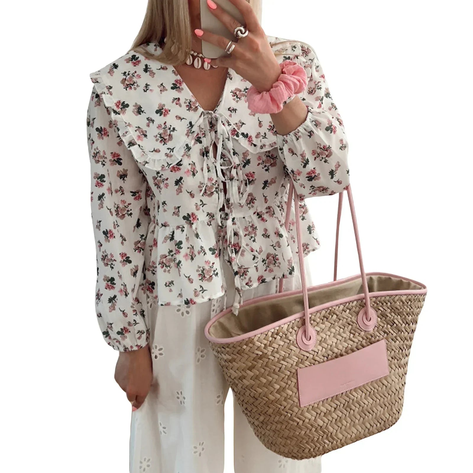 Donna con camicetta floreale bianca, pantaloni bianchi e borsa di paglia rosa. Moda estiva, abbigliamento casual elegante, accessori femminili.