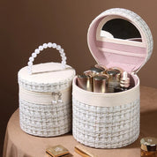 Scatola porta trucchi rotonda in tessuto tweed bianco con manico di perle, specchio interno e scomparti per cosmetici. Elegante e funzionale.