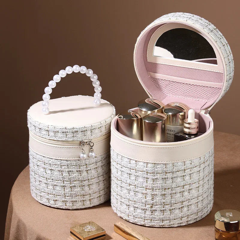 Scatola porta trucchi rotonda in tessuto tweed bianco con manico di perle, specchio interno e scomparti per cosmetici. Elegante e funzionale.