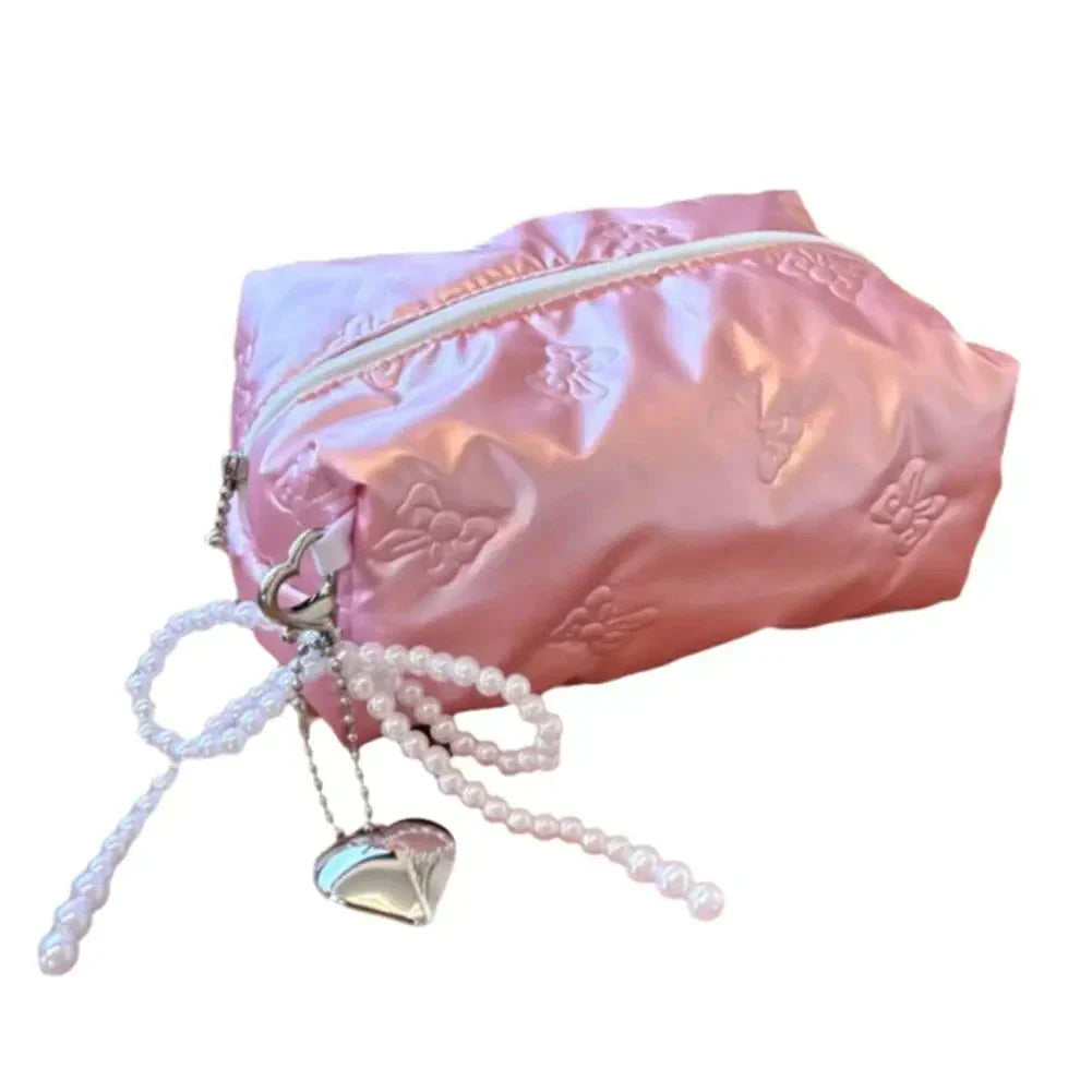 Astuccio rosa in raso con cerniera, decorato con motivi floreali, perline e ciondolo a cuore. Accessorio moda elegante e funzionale.
