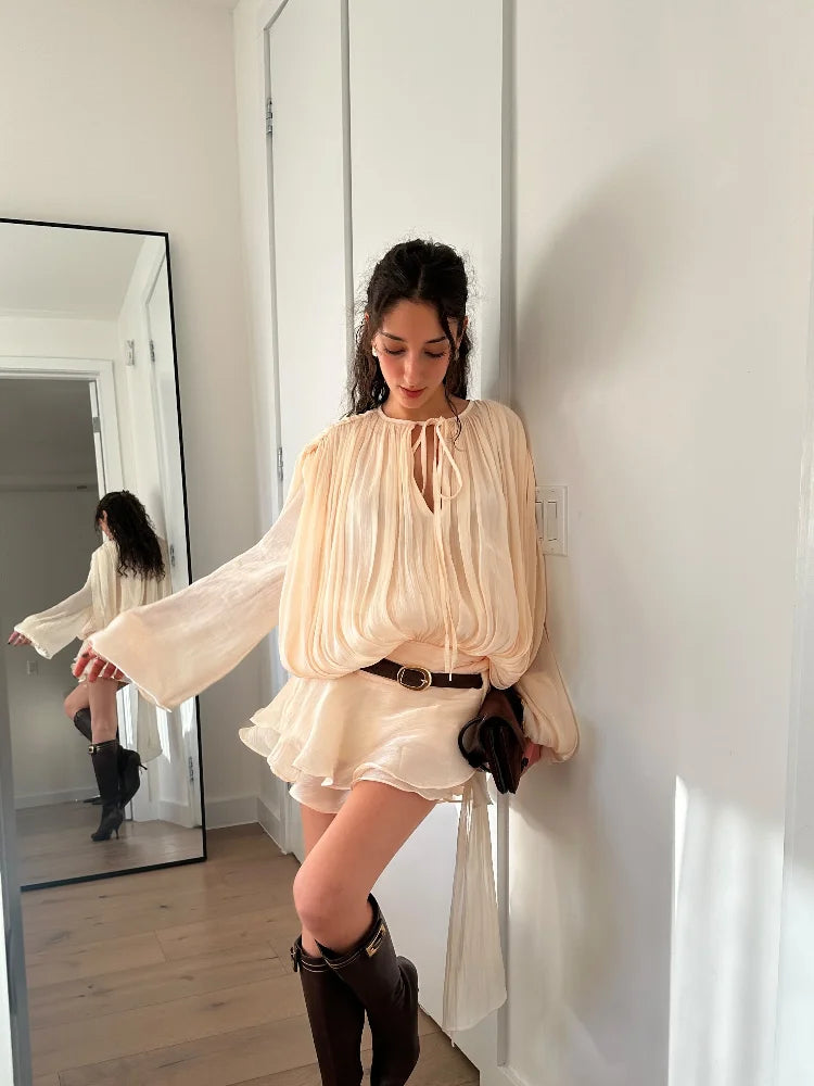 Donna con abito beige trasparente e stivali marroni, posa in un corridoio moderno con specchio. Moda femminile elegante, abbigliamento casual chic.