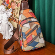 Zaino a tracolla multicolore con motivo geometrico su tavolo di legno, accanto a statua d'angelo e tenda verde. Accessorio moda vivace e moderno.