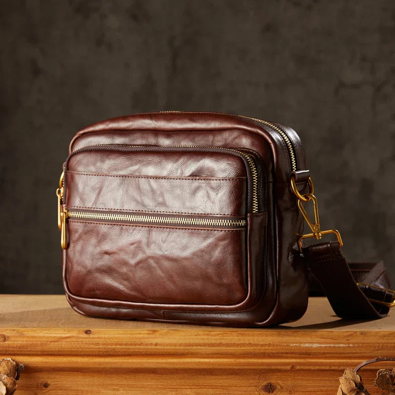 Borsa a tracolla in pelle marrone scuro con cerniere dorate, design elegante e compatto, ideale per uomo, accessorio moda di alta qualità.