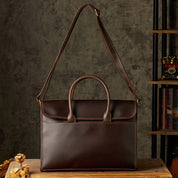 Borsa a tracolla in pelle marrone scuro su tavolo di legno, design elegante e classico, ideale per lavoro e ufficio. Accessorio moda uomo.