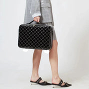 Donna con valigetta nera trapuntata, abito grigio elegante, scarpe con tacco basso. Accessorio moda, stile business chic.