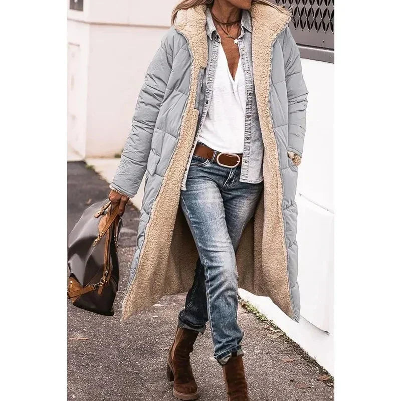 Cappotto lungo imbottito grigio con interno in pelliccia sintetica, indossato con jeans e stivali marroni. Look casual autunnale. Moda donna inverno.