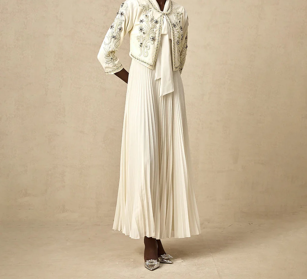 Abito lungo bianco elegante con giacca ricamata, maniche a tre quarti, gonna plissettata, scarpe con tacco. Moda femminile sofisticata.