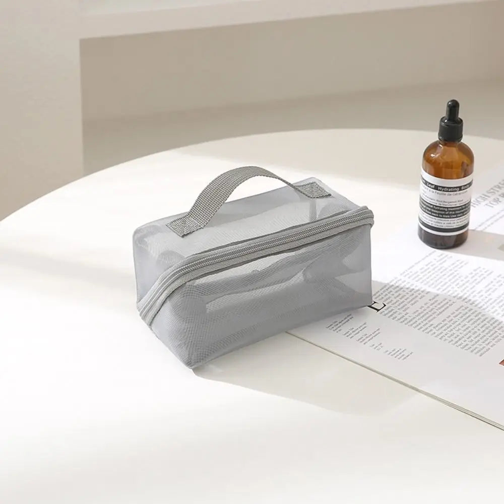 Borsa trasparente grigia su tavolo bianco con flacone di vetro marrone. Ideale per cosmetici, viaggio, organizzazione. Design moderno e funzionale.