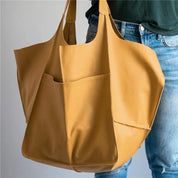Borsa shopper in pelle marrone chiaro, design moderno, tasche esterne, indossata da persona in jeans. Accessorio moda versatile ed elegante.