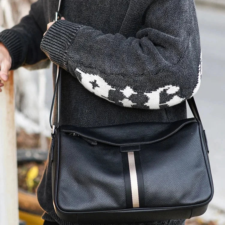 Borsa a tracolla in pelle nera con striscia centrale, indossata da persona con maglione grigio. Accessorio moda elegante e versatile per uomo.