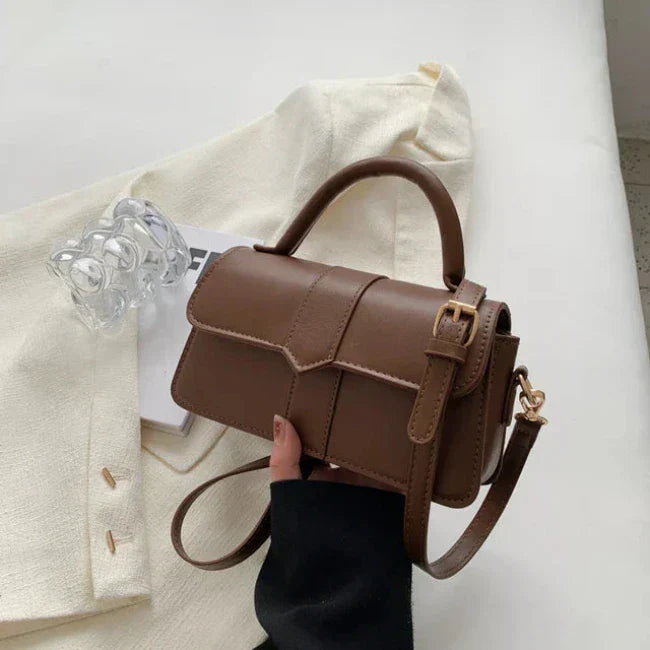 Borsa a tracolla in pelle marrone su giacca bianca, design elegante con fibbia dorata, perfetta per moda donna e accessori di tendenza.