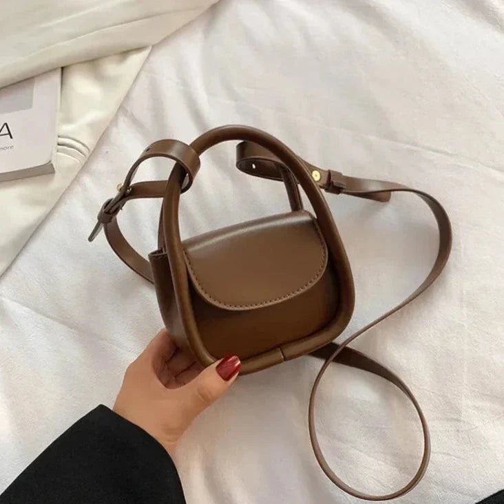 Borsa a tracolla in pelle marrone su letto bianco, design compatto e moderno, ideale per moda femminile. Accessorio elegante e versatile.