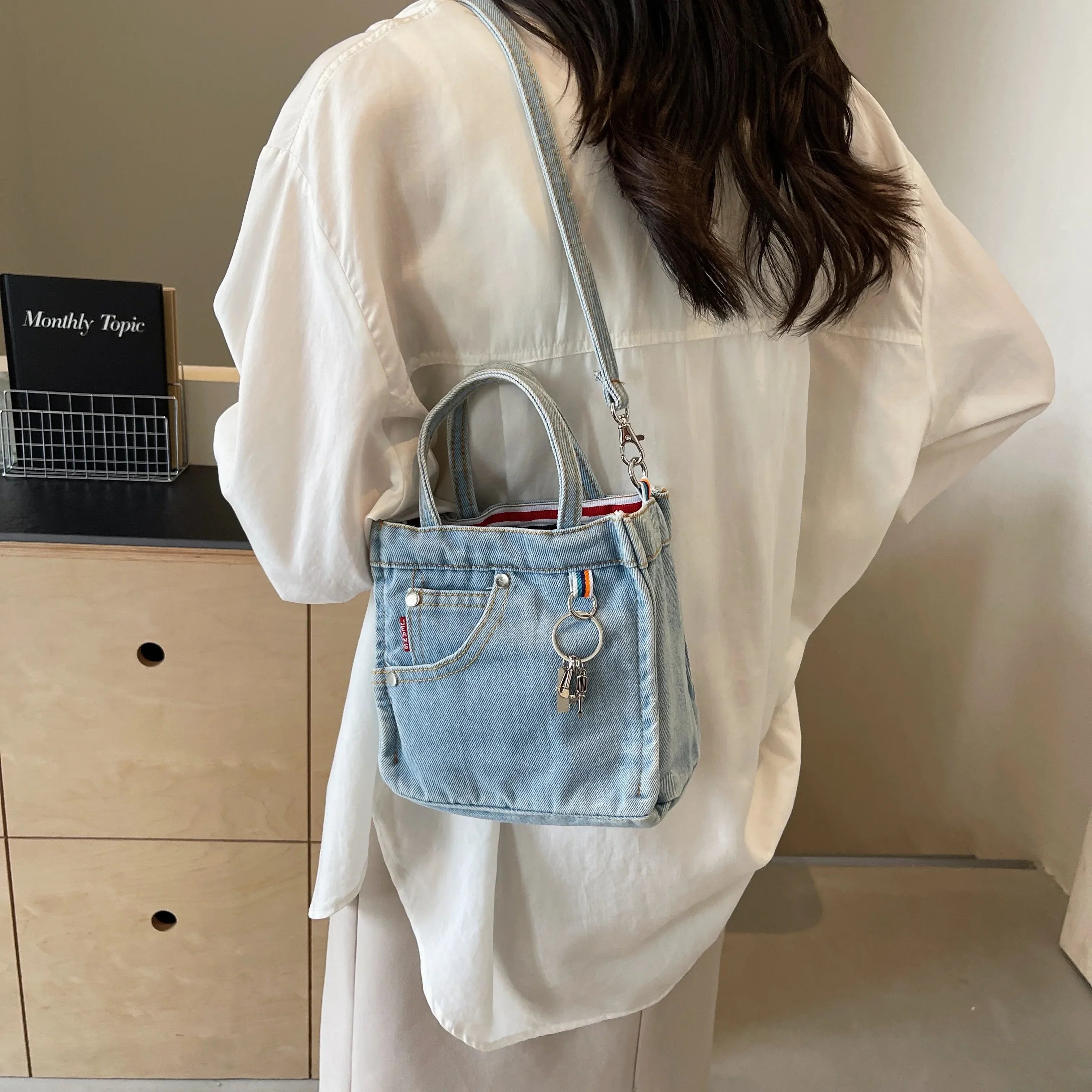 Donna con camicia bianca indossa borsa a tracolla in denim con tasca frontale e portachiavi. Stile casual, moda femminile, accessori trendy.