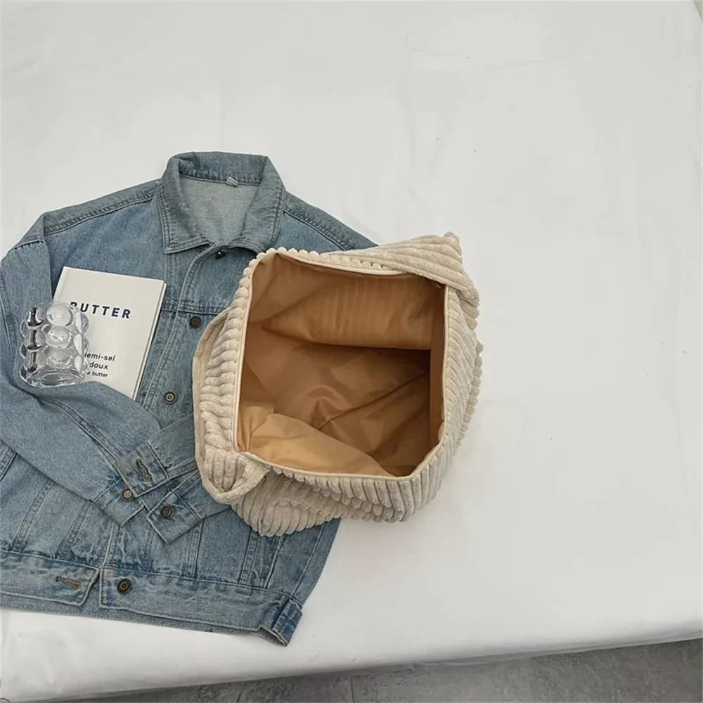 Giacca di jeans blu con libro e cartone di uova su tavolo bianco, accanto a borsa beige aperta. Accessori moda casual, stile urbano.