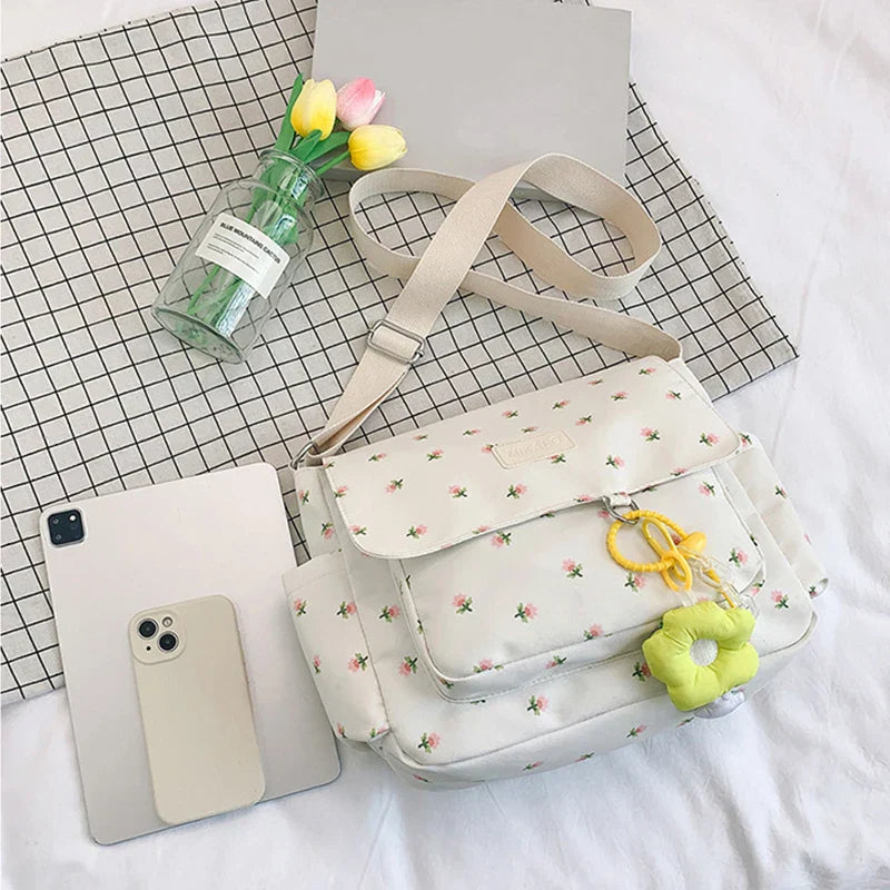 Borsa a tracolla floreale bianca con charm giallo, affiancata da un iPhone e un iPad su tovaglia a quadri, vaso di tulipani colorati.