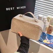Borsa cosmetica beige con glitter, manico superiore, chiusura a zip, su sfondo con prodotti di bellezza. Elegante e pratica per viaggi.