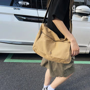 Donna con borsa a tracolla beige in tessuto, davanti a un'auto bianca. Moda casual, accessori femminili, stile urbano.