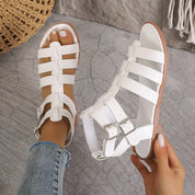 Sandali gladiatore bianchi da donna, cinturini incrociati, fibbie regolabili, suola in gomma, indossati con jeans. Scarpe estive eleganti e casual.