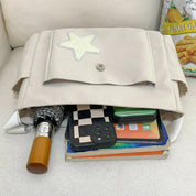 Zaino beige aperto con stella, contenente ombrello, libri, scacchiera, smartphone e snack al limone. Accessori per scuola e viaggio.