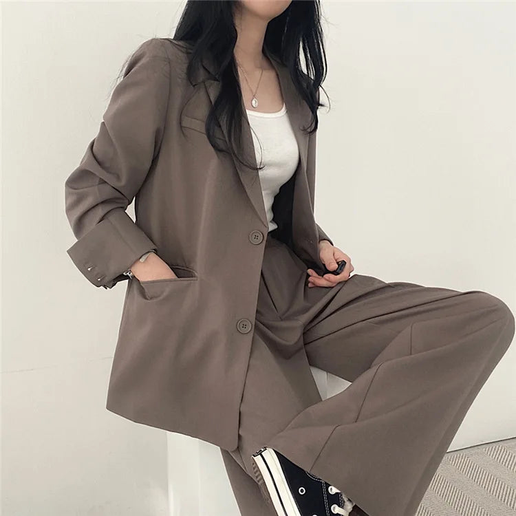 Donna in abito elegante marrone, giacca e pantaloni, con top bianco e sneakers nere. Moda casual chic, abbigliamento femminile moderno.