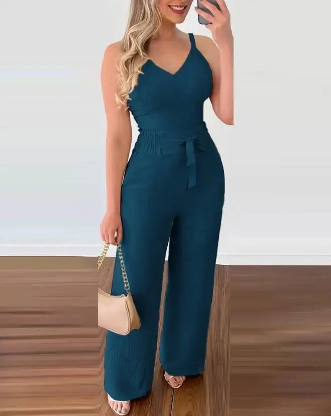 Donna in tuta blu elegante, senza maniche, con cintura in vita, borsa beige a tracolla, sandali. Moda femminile, abbigliamento estivo chic.
