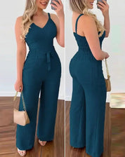 Tuta elegante donna blu scuro, senza maniche, con cintura in vita, pantaloni larghi, abbinata a sandali beige e borsa a tracolla.